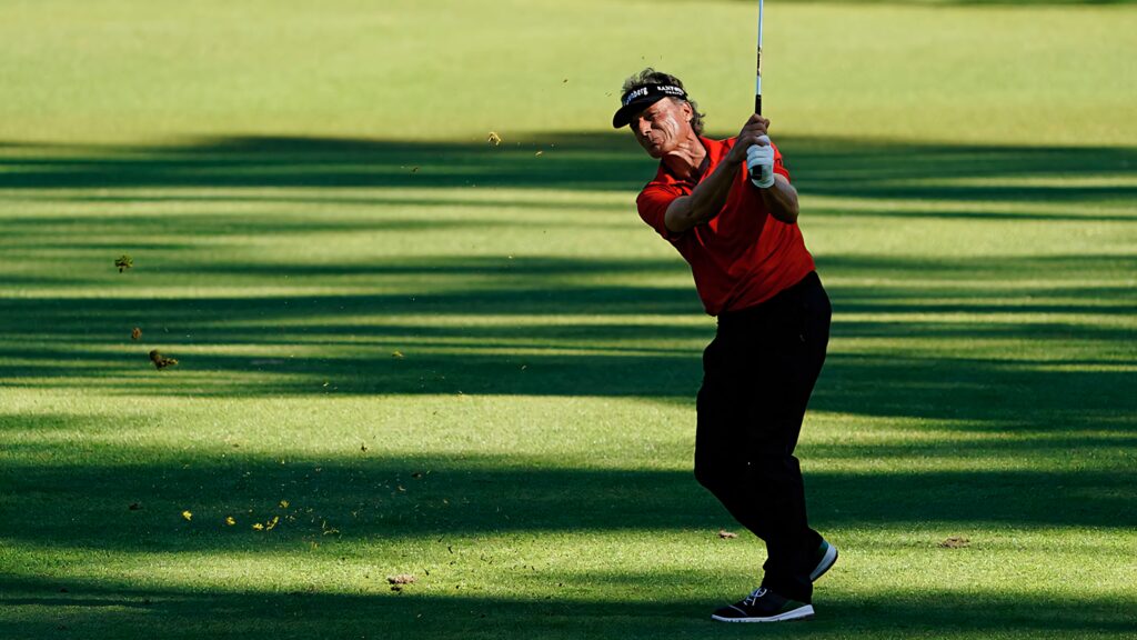 Bernhard Langer swinging golf club on sunlit course with vibrant green grass and shadows Wallpaper