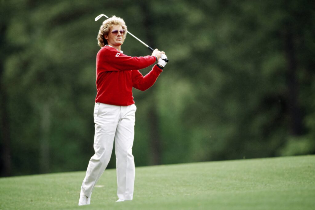 Bernhard Langer in red sweater perfecting golf swing on lush green course wallpaper background