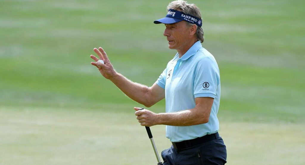 Bernhard Langer side view on golf course holding putter raising hand in light blue shirt Wallpaper
