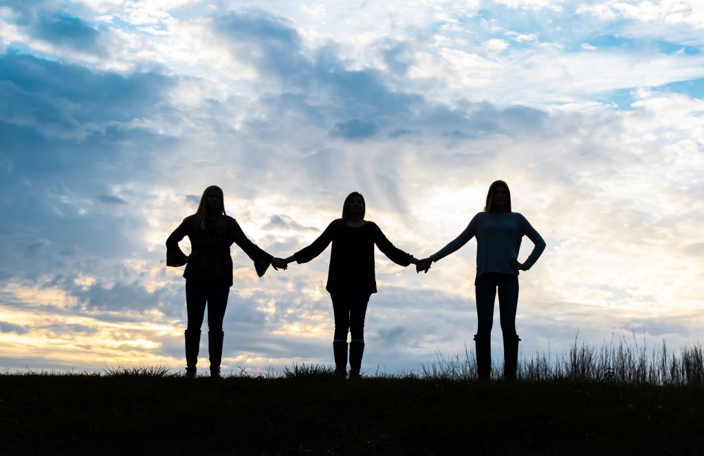 Three friends holding hands silhouette sunset sky grassy hilltop friendship wallpaper background