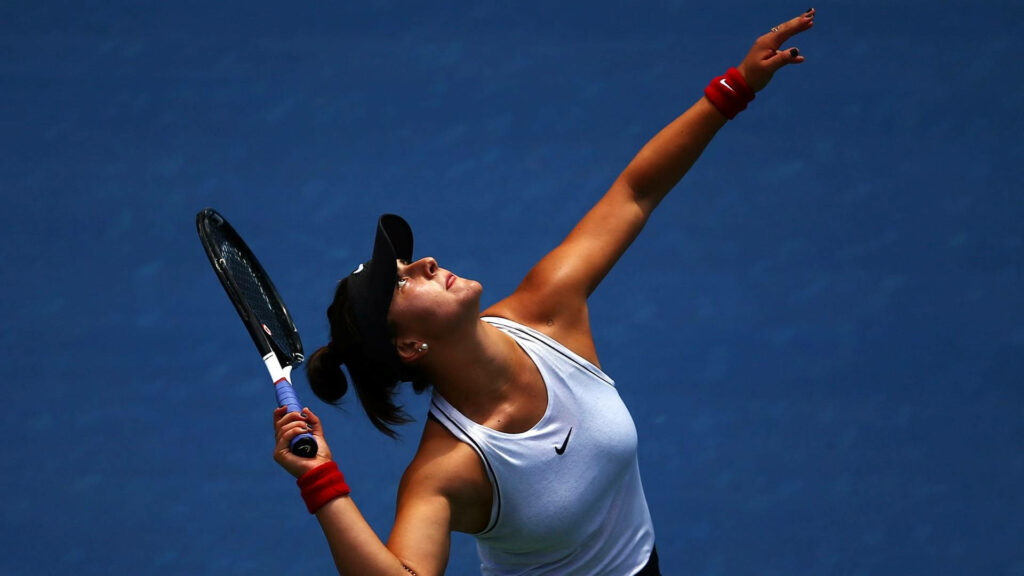 Bianca Andreescu focused preparing to serve on tennis court with deep blue wallpaper background