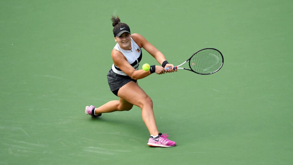 Bianca Andreescu hitting a two handed backhand on green tennis court intense focus action shot Wallpaper