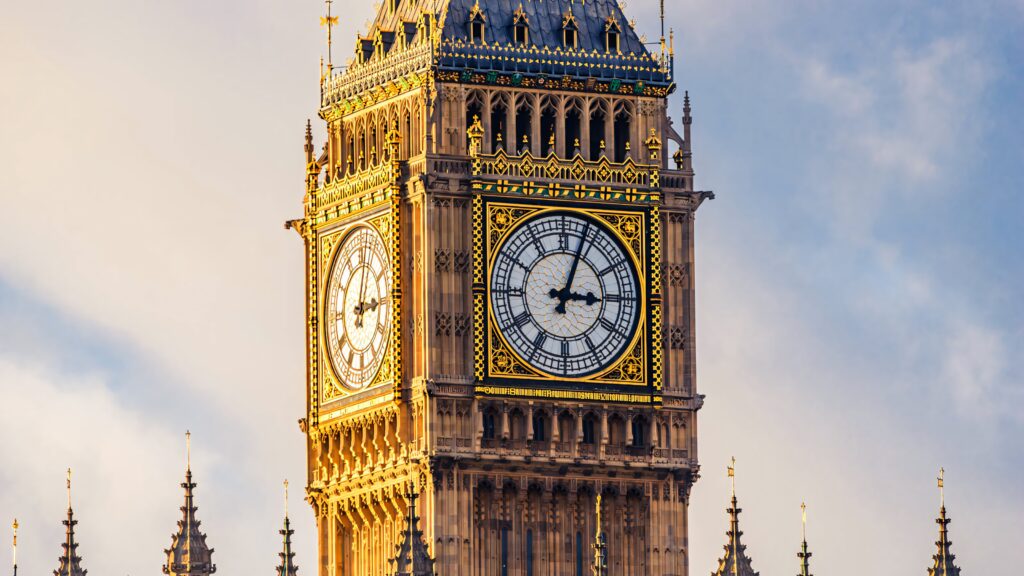 Big Ben close-up glowing in golden afternoon light with detailed clock faces and cloudy sky background Wallpaper