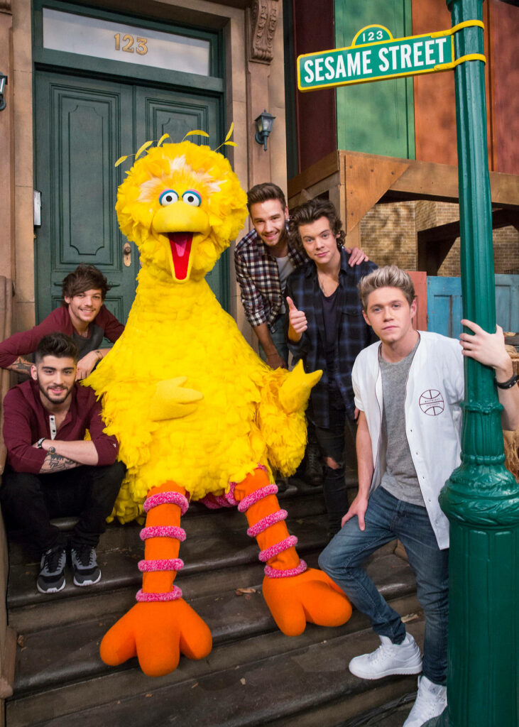 Big Bird with One Direction on Sesame Street in front of iconic green doors cheerful group Wallpaper
