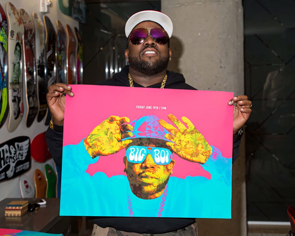 Big Boi holding vibrant concert poster with colorful artwork in front of skateboard deck wall Wallpaper