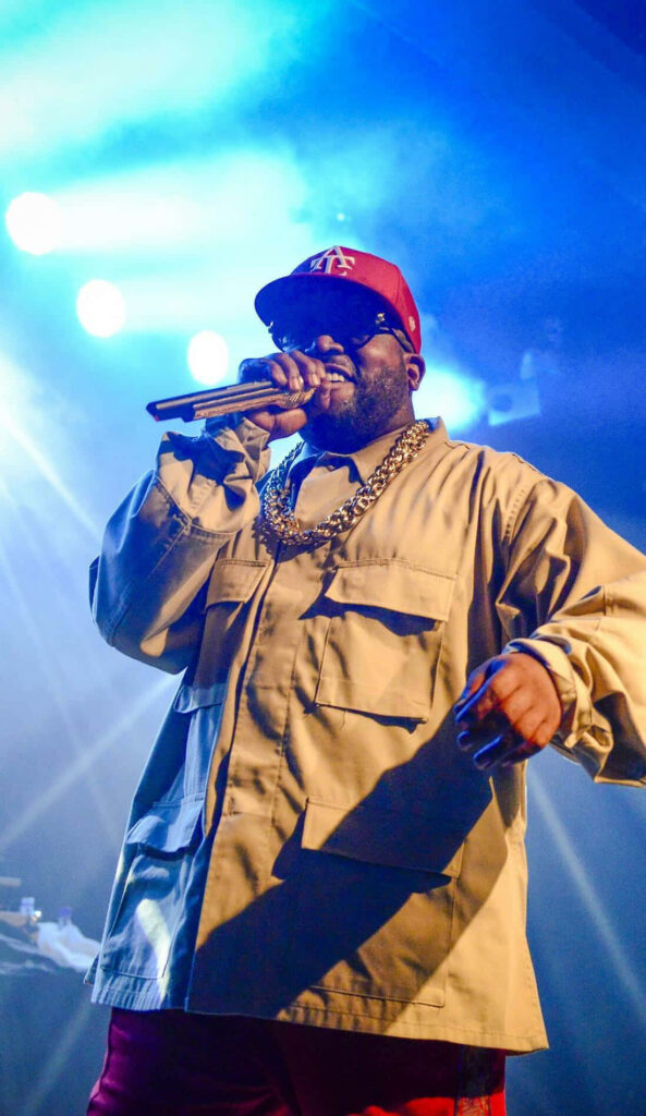 Big Boi performing confidently on stage with vibrant lights wearing chain cap and stylish outfit Wallpaper