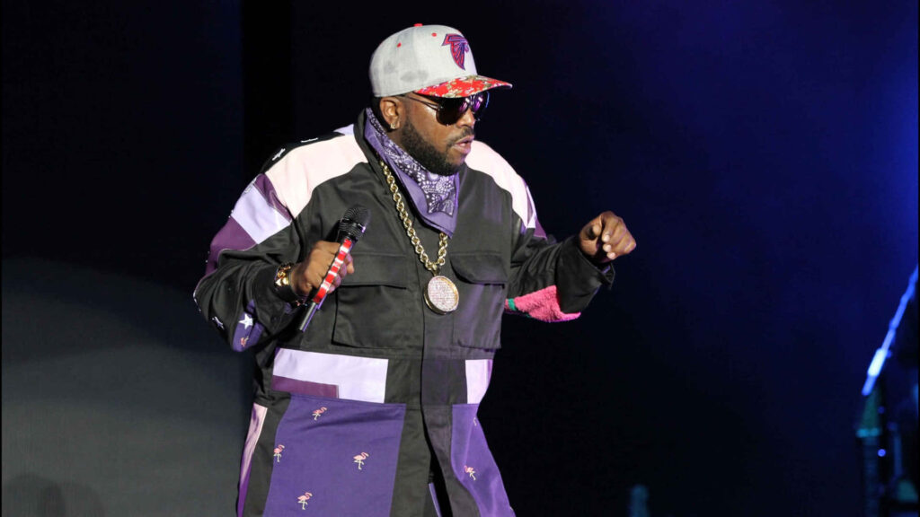 Big Boi performing on stage in stylish jacket and hat with dramatic lighting and dark background Wallpaper