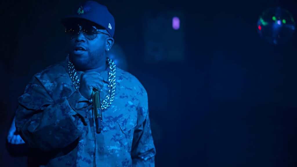 Big Boi performing live wearing camouflage jacket and gold chain under blue stage lighting Wallpaper