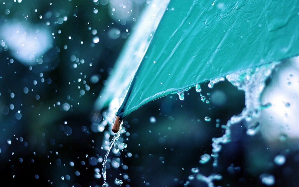 Close-up of vibrant teal umbrella with water droplets splashing in heavy rain QHD wallpaper background
