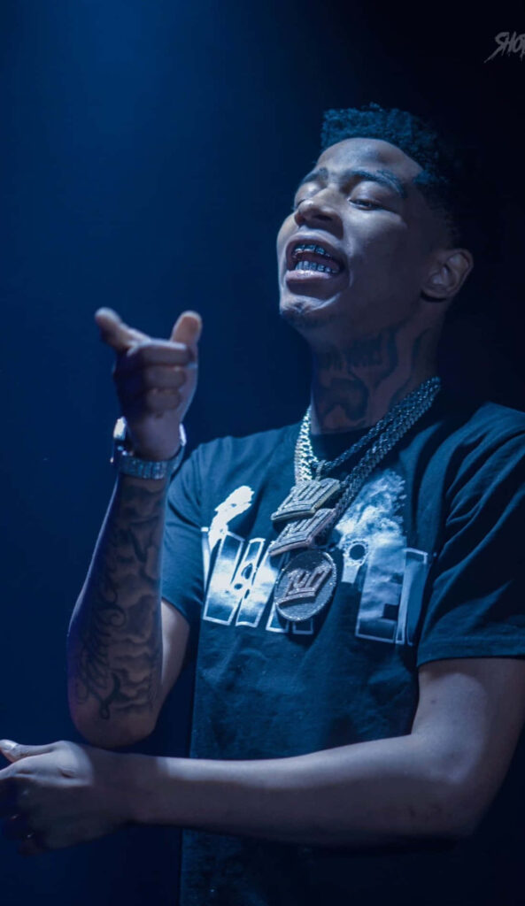Big Scarr performing on stage with tattoos jewelry and blue lighting wallpaper background