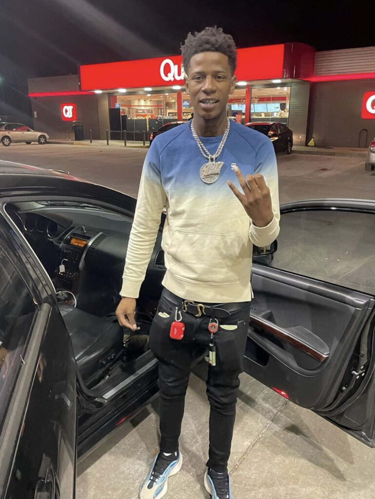 Big Scarr by car at night wearing chains and stylish outfit outside QuikTrip capturing rapper vibe Wallpaper