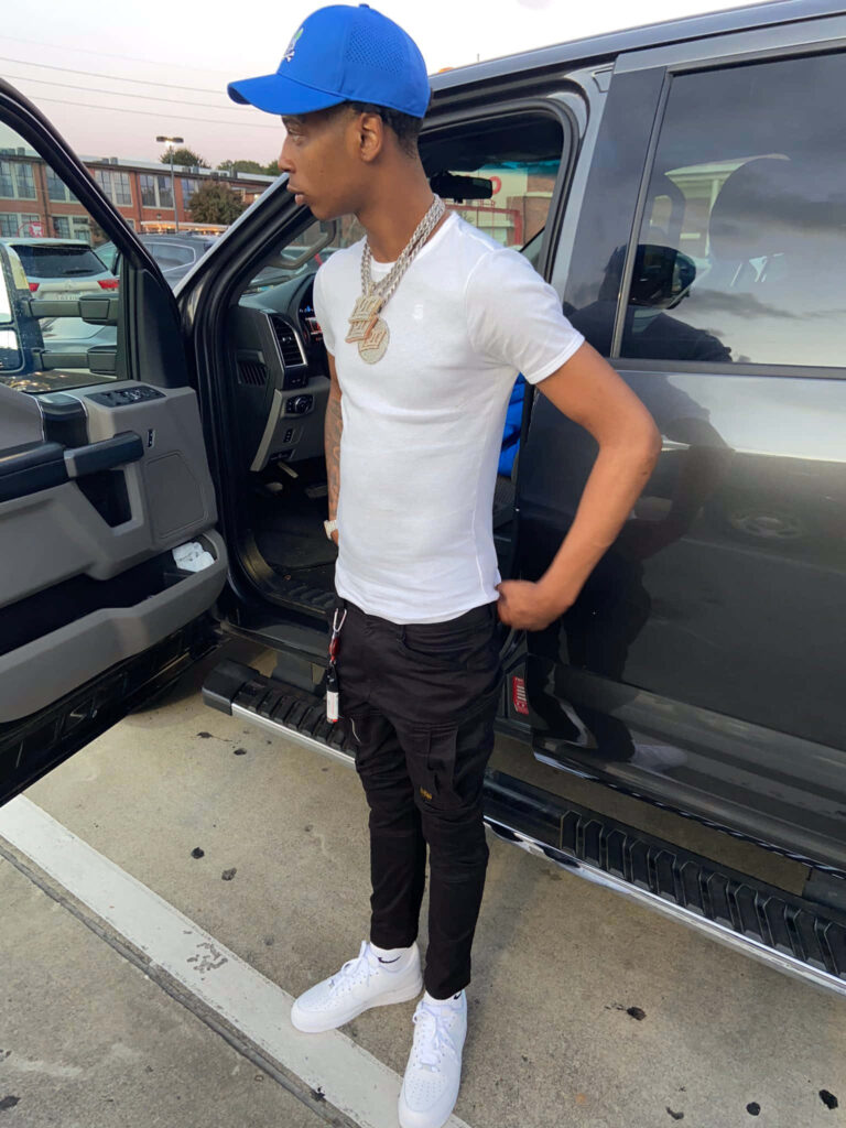 Big Scarr rapper in blue cap white tee black pants white sneakers next to black car wallpaper background