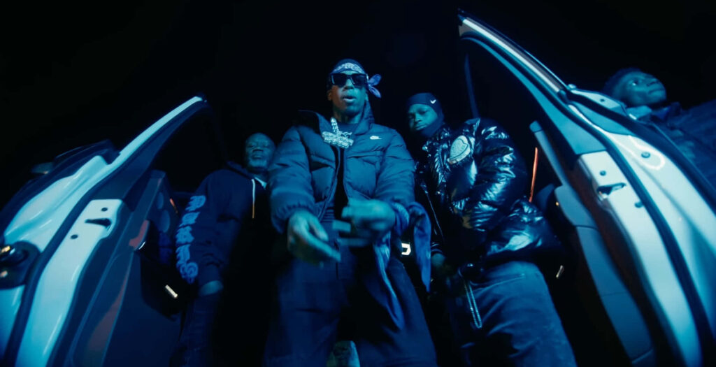 Big Scarr in stylish streetwear between open car doors at night with his crew urban vibe wallpaper