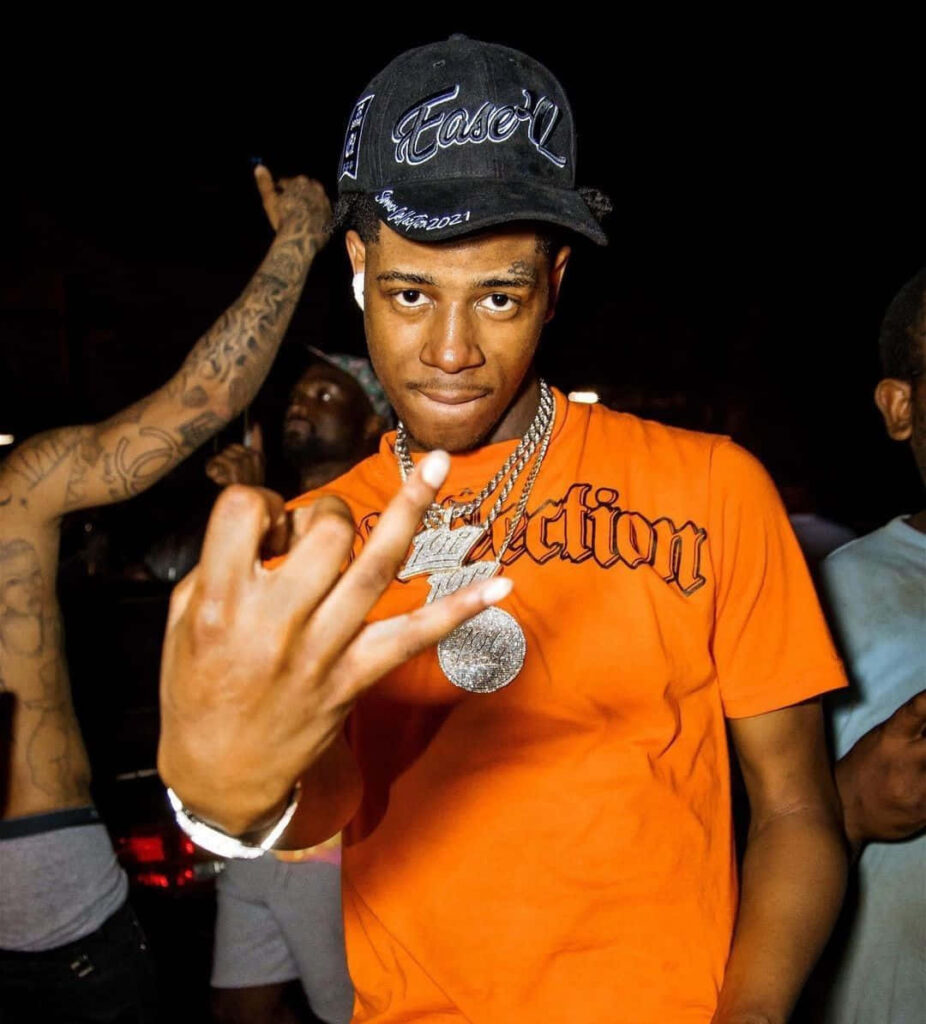 Big Scarr in orange shirt and flashy jewelry vibrant American rapper lifestyle nighttime backdrop Wallpaper