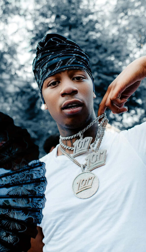 Big Scarr wearing signature chains and streetwear in vibrant wallpaper background pose