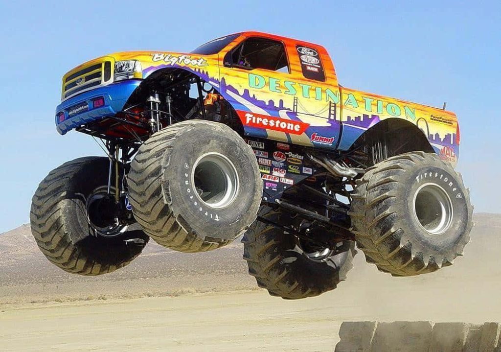 Bigfoot monster truck mid-air jump with vibrant cityscape livery over desert background Wallpaper