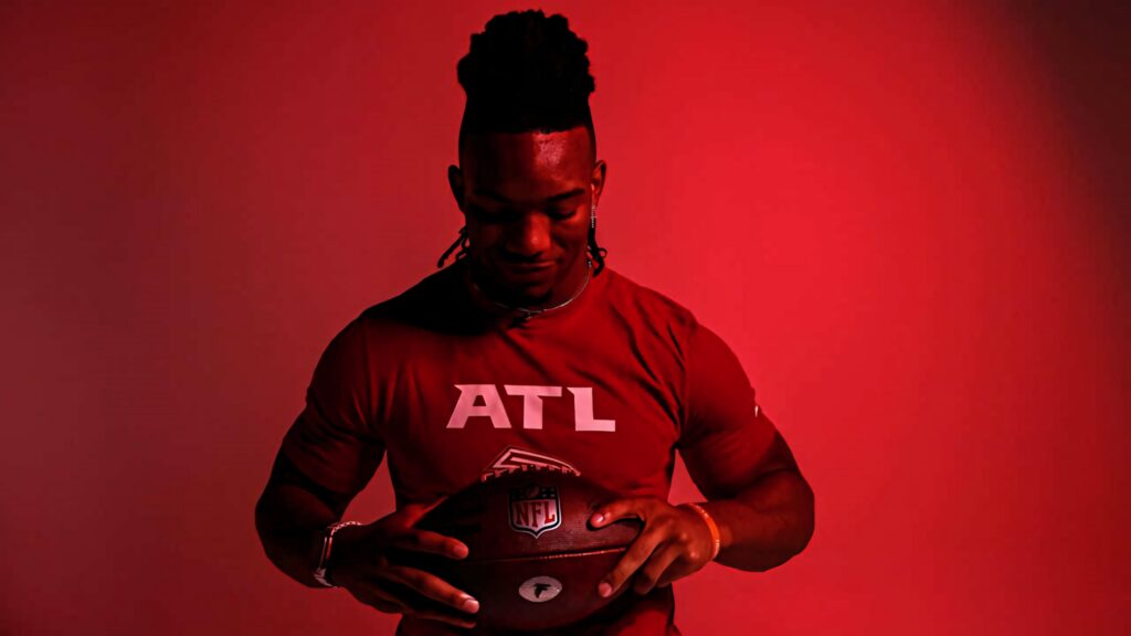 Bijan Robinson in Atlanta Falcons shirt holding football red background football wallpaper
