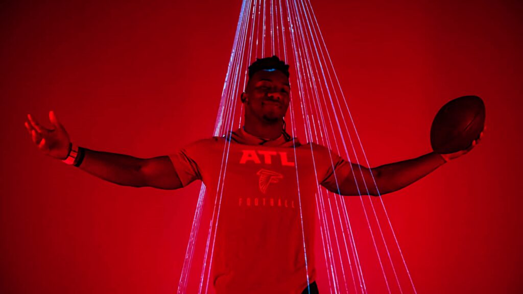 Bijan Robinson in Atlanta Falcons shirt holding football under red lights dynamic wallpaper background