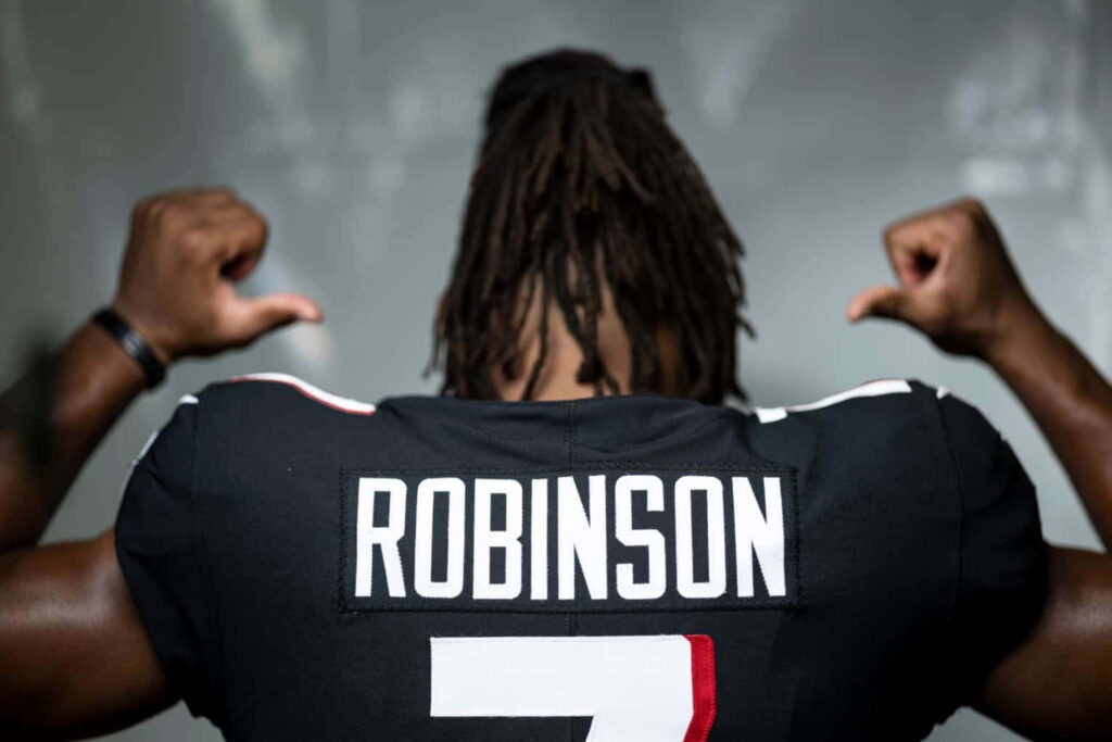 Bijan Robinson flexing muscles wearing football jersey number 7 with name and wallpaper background