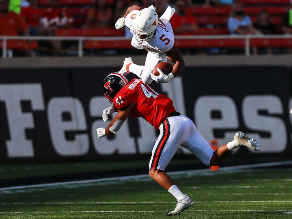 Bijan Robinson leaps over defender in dynamic college football action showing athleticism and skill Wallpaper
