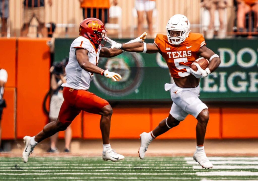 Bijan Robinson of Texas running with football evading defender in intense college football game Wallpaper