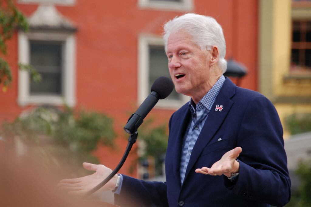 Bill Clinton delivering energetic outdoor speech with expressive gestures colorful urban backdrop Wallpaper