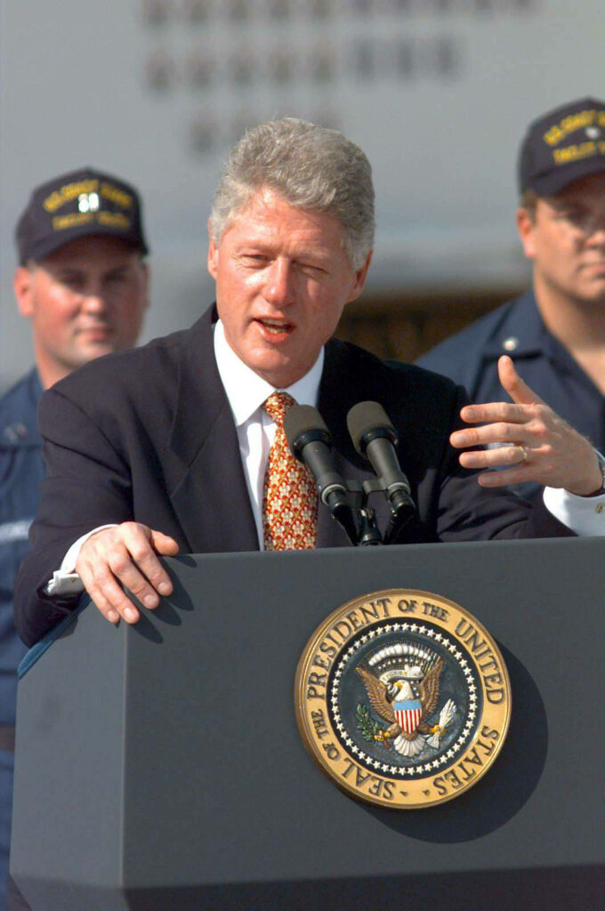 Bill Clinton speaking at presidential podium with US seal and uniformed officers behind him Wallpaper