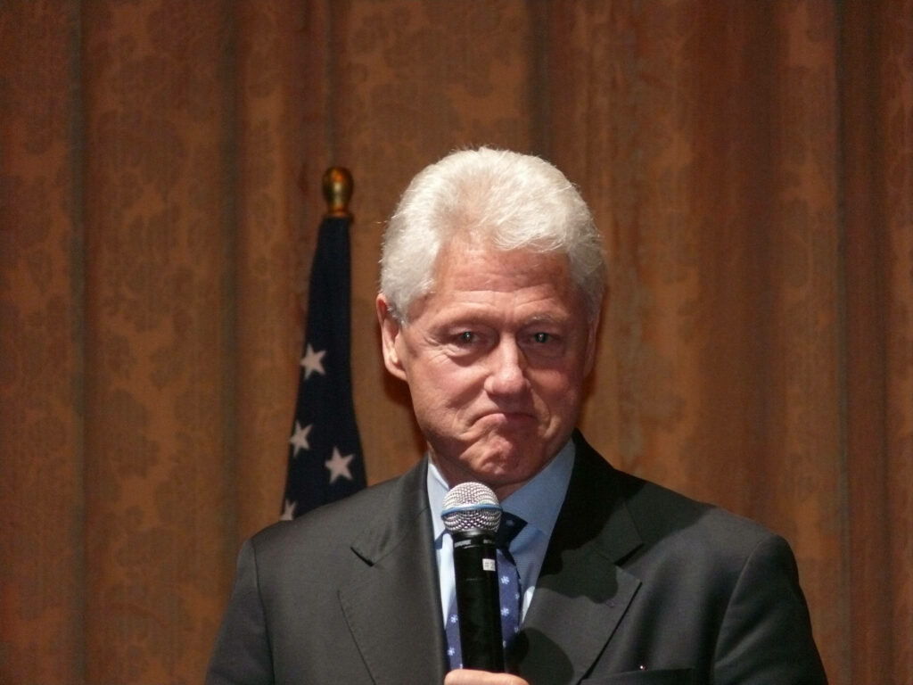 Bill Clinton speaking in suit with thoughtful expression American flag background wallpaper