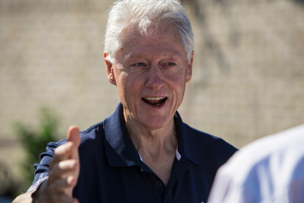 Close-up portrait of Bill Clinton smiling warmly and extending hand with blurred outdoor background Wallpaper