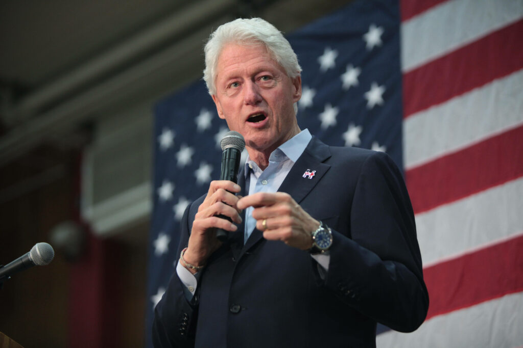 Bill Clinton speaking into microphone with large USA flag patriotic wallpaper background