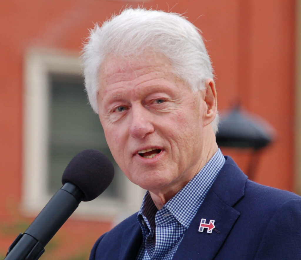 Portrait of former President Bill Clinton speaking into microphone outdoors with blurred background Wallpaper