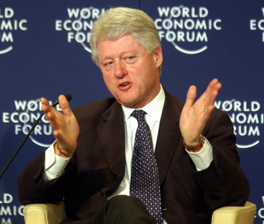 Bill Clinton speaking passionately at World Economic Forum session with logo in background wallpaper