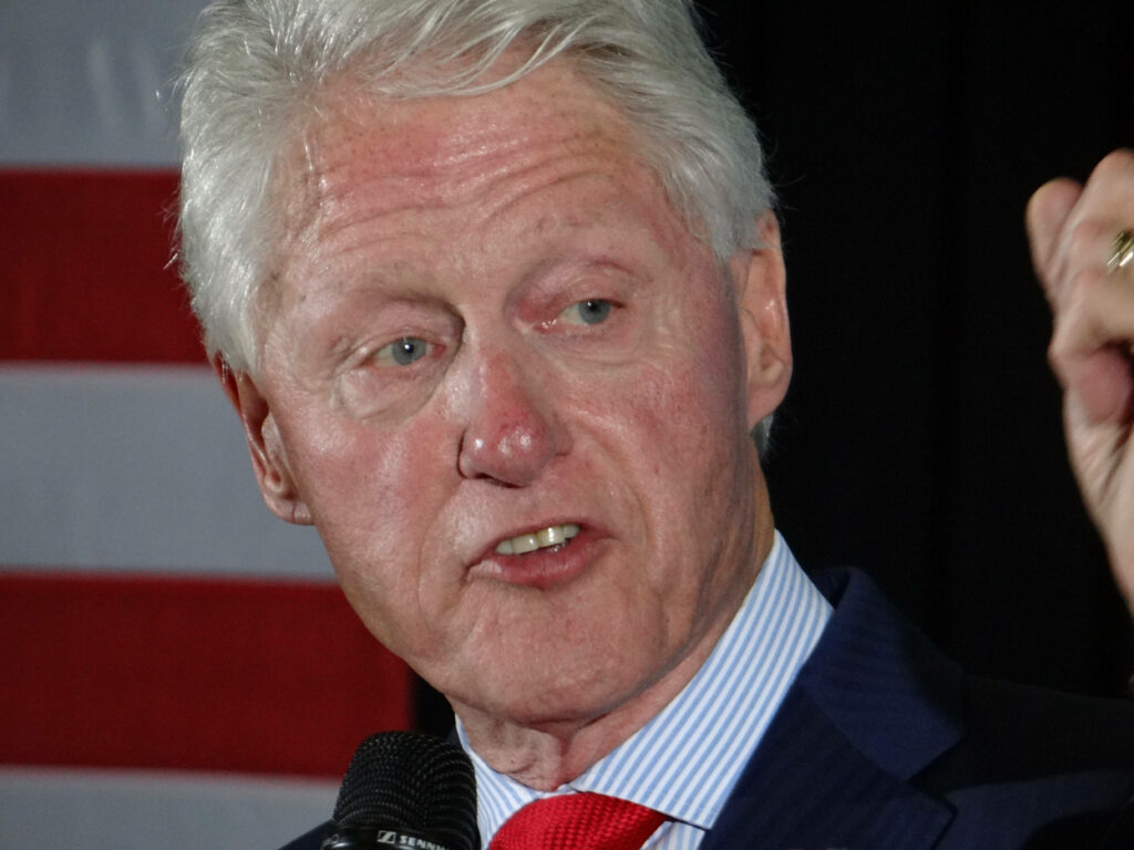 Bill Clinton speaking with focused expression American flag backdrop candid political wallpaper