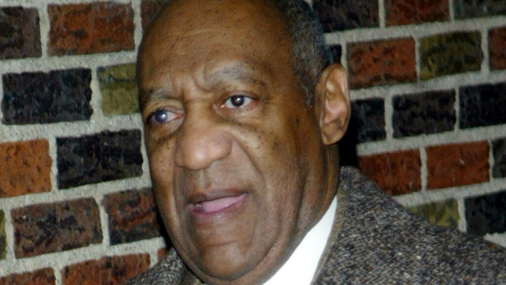 Bill Cosby with concerned expression standing against textured brick wall background wallpaper