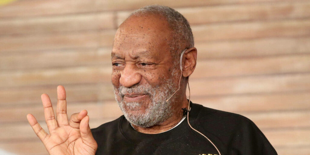 Bill Cosby smiling and gesturing in black sweatshirt with blurred background wallpaper
