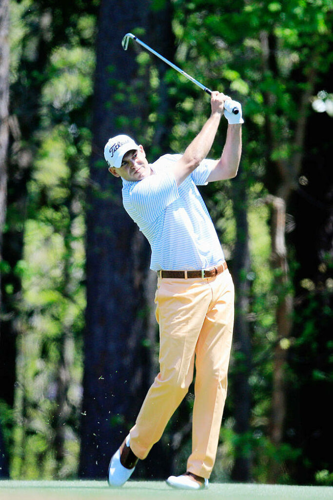 Bill Haas mid-swing on lush golf course with tall green trees focused golf wallpaper background