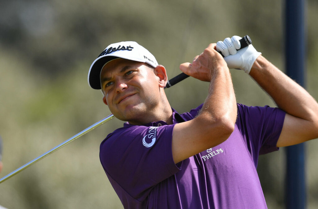 Bill Haas mid golf swing wearing purple shirt and white cap dynamic golf course wallpaper