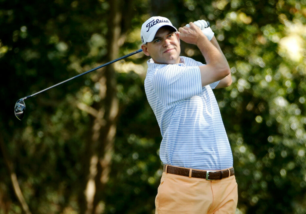 Bill Haas mid-swing on lush golf course showing focus and athletic skill with tree background Wallpaper