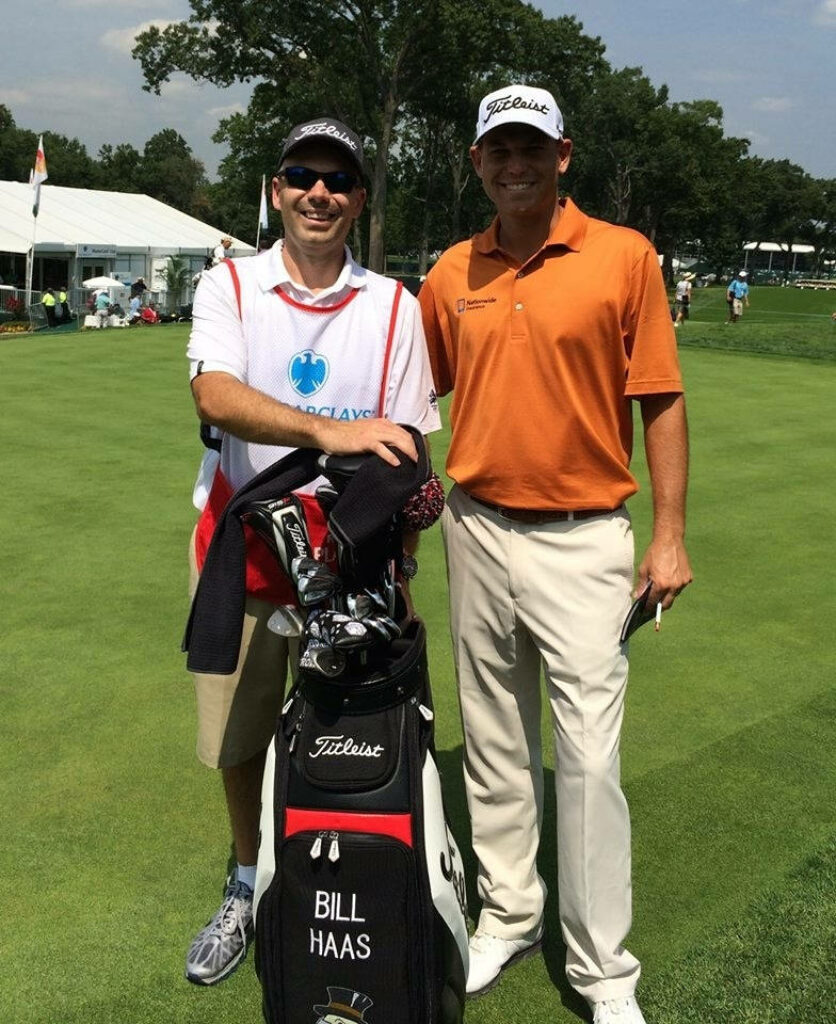 Bill Haas and caddie smiling on golf course near golf bag with Haas name in lush tournament setting Wallpaper