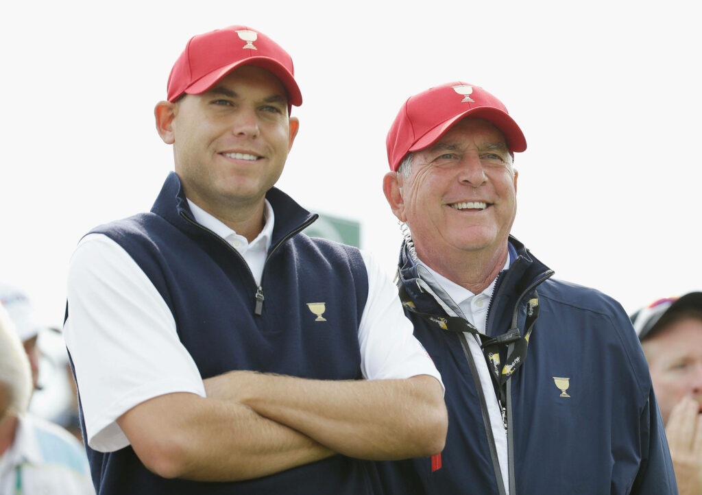 Bill Haas and Jay Haas side by side in matching golf outfits and red caps on golf course Wallpaper