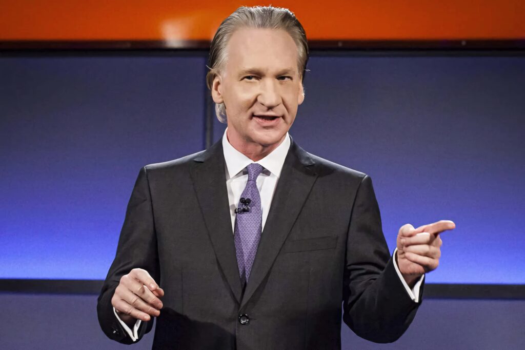 Bill Maher speaking confidently in suit and tie with modern studio wallpaper background