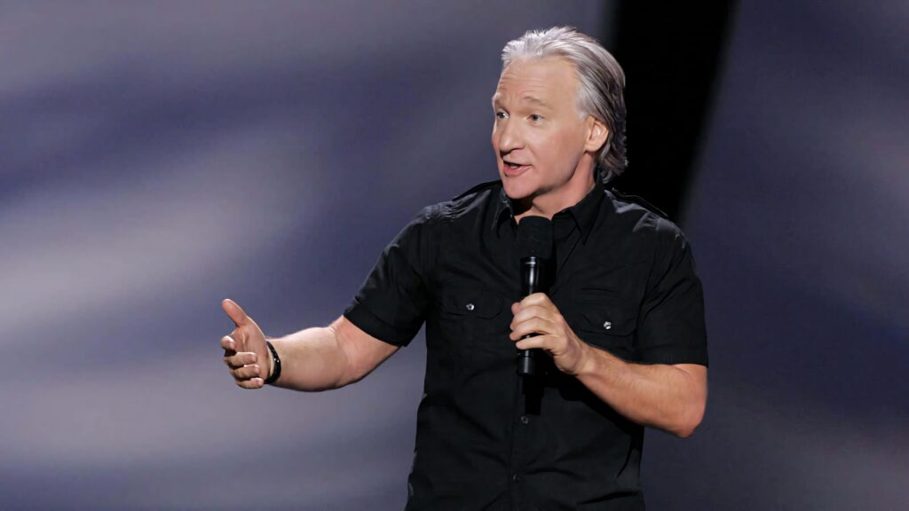 Bill Maher delivers sharp comedic commentary on stage in black shirt with dynamic gestures wallpaper