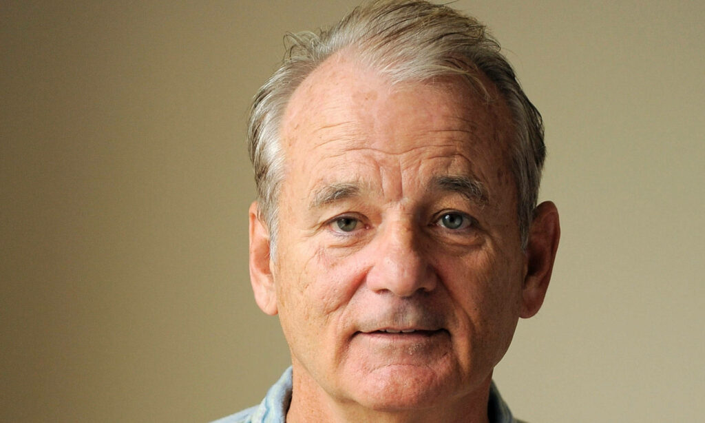 Close-up portrait of Bill Murray with signature expression on a simple neutral wallpaper background