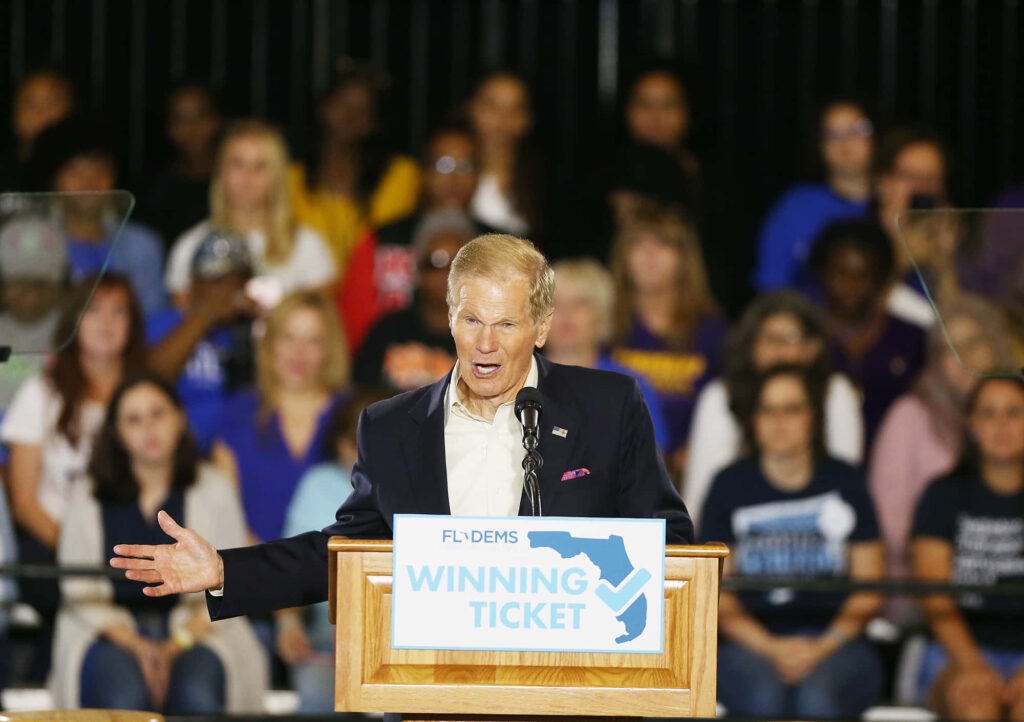 Bill Nelson speaking at rally podium with Winning Ticket sign diverse audience behind him wallpaper