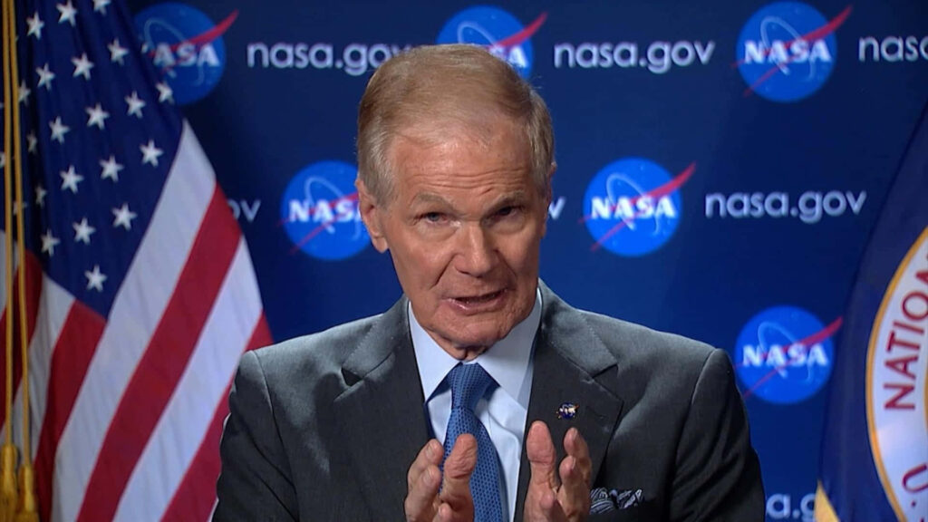 Bill Nelson speaking for NASA with American flag and NASA logo in official blue-themed setting Wallpaper