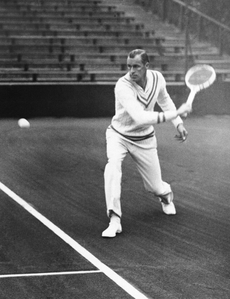 Tennis legend Bill Tilden poised in action on classic court with vintage stands background wallpaper