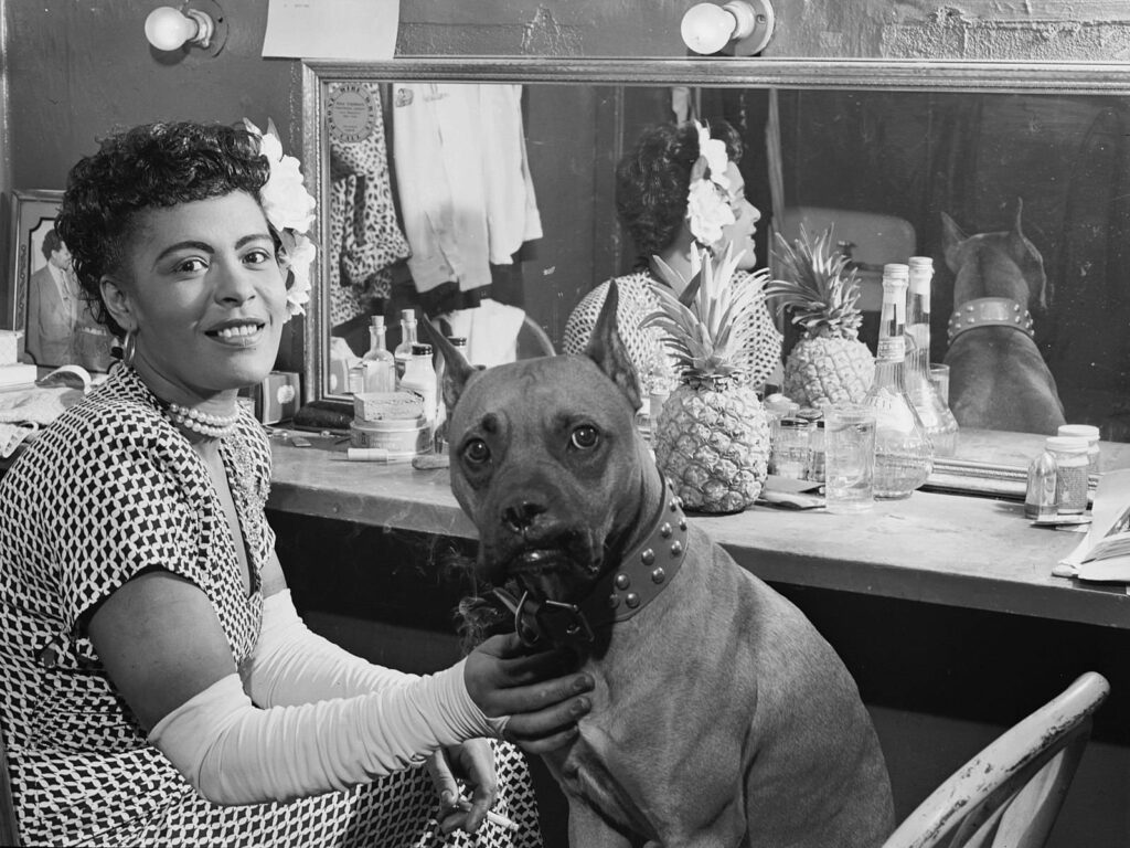Billie Holiday smiles backstage posing with her loyal dog in front of a mirror intimate moment Wallpaper