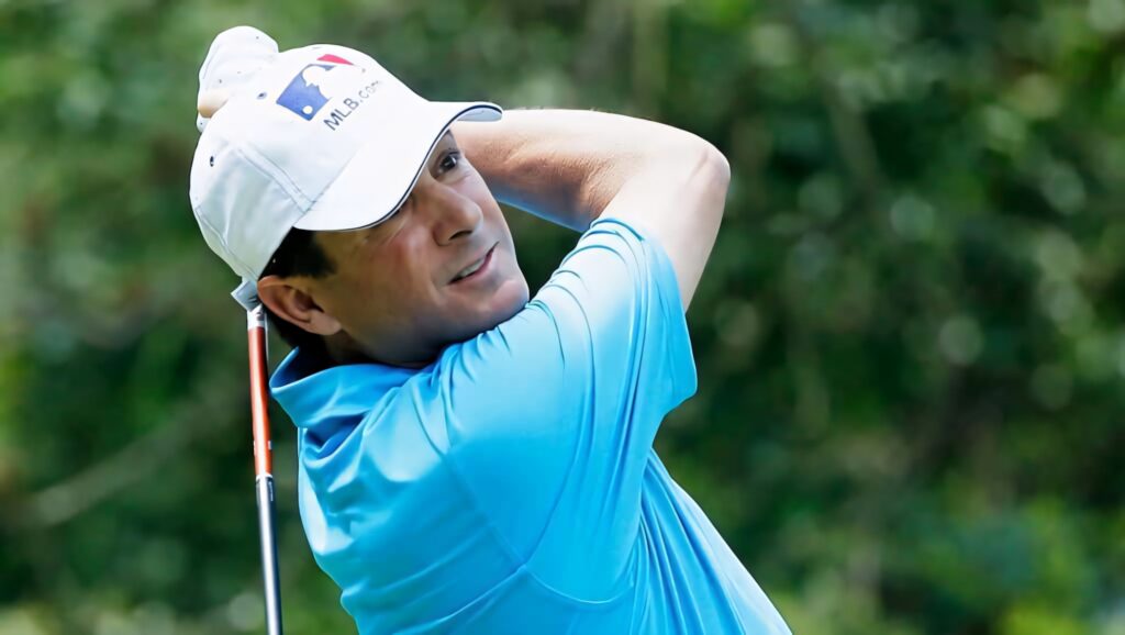 Billy Andrade mid-swing on golf course wearing light blue shirt white cap bright daylight golf background Wallpaper