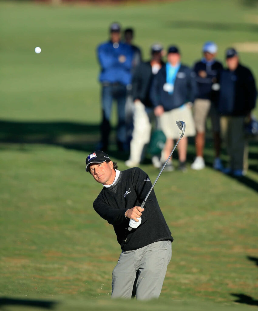 Billy Andrade mid-swing on golf course focused follow through golf shot with spectators background Wallpaper
