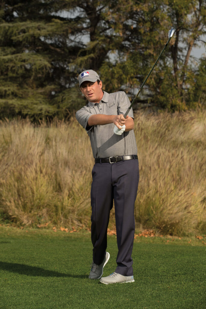 Golfer Billy Andrade mid swing on lush green golf course with scenic trees background wallpaper